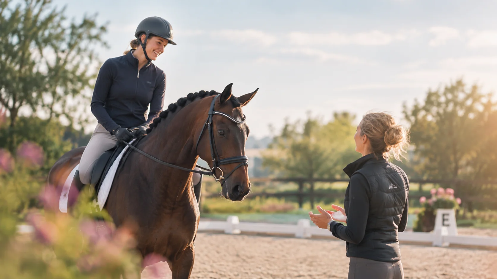 Een ruiter te paard in gesprek met haar instructeur op de dressuurbaan